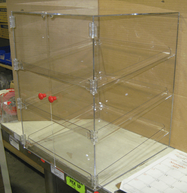 Clear acrylic display case with shelves and red knobs on a warehouse shelf