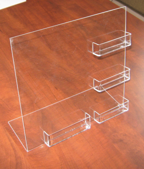 Clear acrylic display stand with three horizontal shelves on a wood table