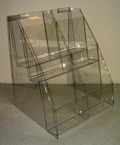 Clear acrylic display rack with three angled shelves against a plain wall