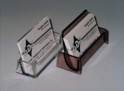 Two business cards in clear plastic holders, one clear and one dark brown, on a light surface.