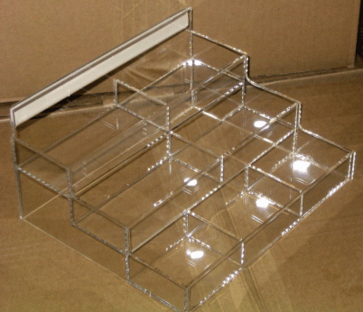Clear acrylic stepped display organizer with multiple small compartments on a cardboard background