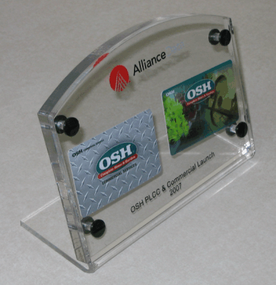 Clear acrylic desk plaque holding two OSH business cards with “Alliance” text on top