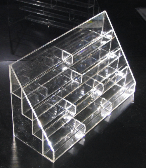 Clear acrylic countertop display rack with multiple small compartments, shown at an angle on a dark background