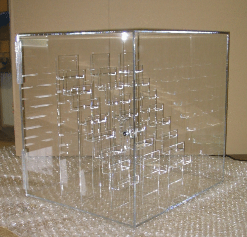 Clear acrylic cube with stepped internal geometric patterns on a beige surface