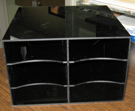 Black glossy desktop organizer with six cubby compartments on a wooden surface.