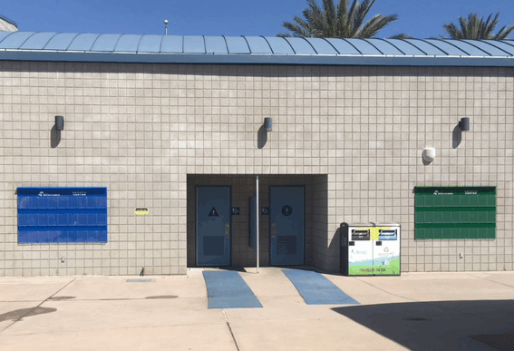 Exterior of a small public building with blue and green mailboxes beside a glass entrance door