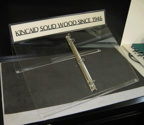 Clear acrylic display case with a metal hinge and a sign reading “Kincaid Solid Wood Since 1948.”