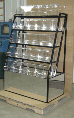 Black metal wire display rack with clear shelves on a wooden pallet in a warehouse.