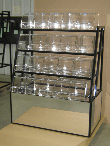 Clear glass cups arranged on a black metal display shelf in a store or café, with an empty lower compartment
