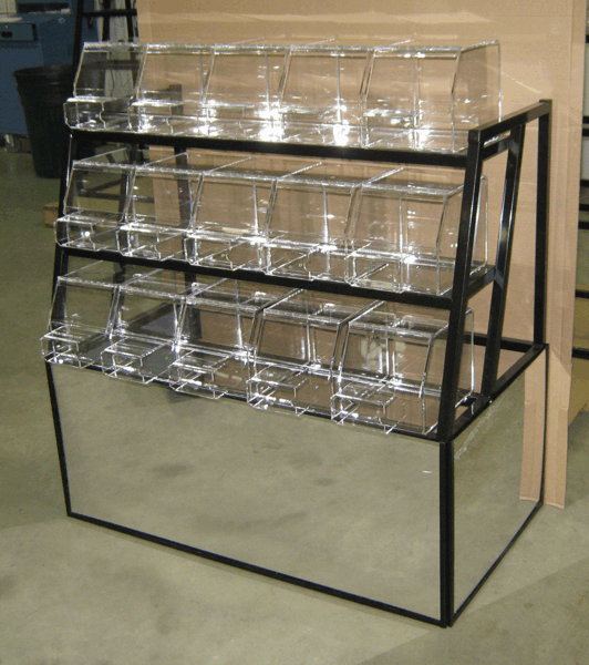 Black metal rack holding rows of clear plastic display bins in a warehouse-like setting