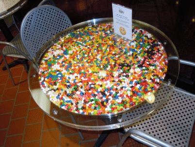 Large round tray of colorful candy on a café table with metal chairs nearby