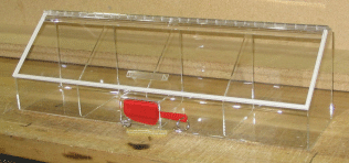 Clear plastic mouse cage with a red latch on a wooden surface