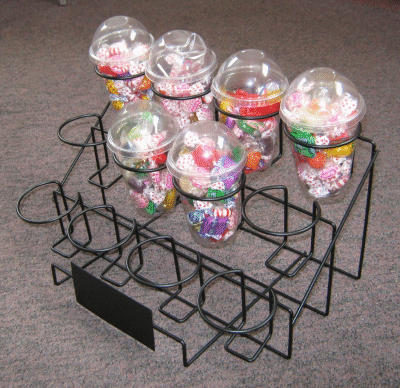 Wire candy dispenser rack with six clear globe jars on a carpeted floor