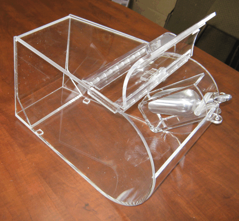 Clear acrylic mechanical device on a wooden table, with a boxy frame and curved front section