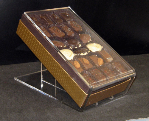 Display box of assorted chocolates with a clear slanted lid on a stand