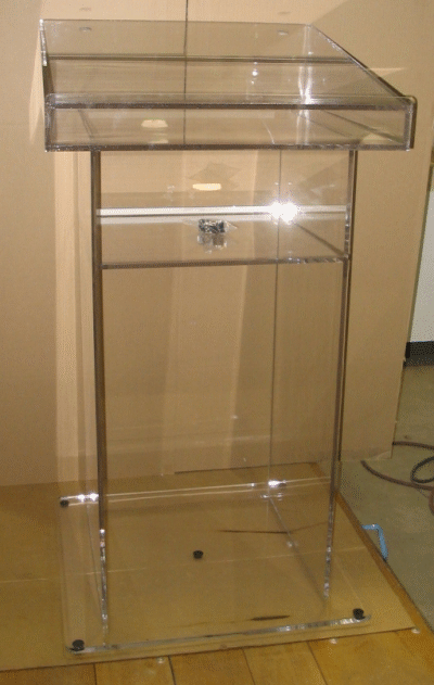 Clear acrylic podium or lectern with glass shelves against a beige wall