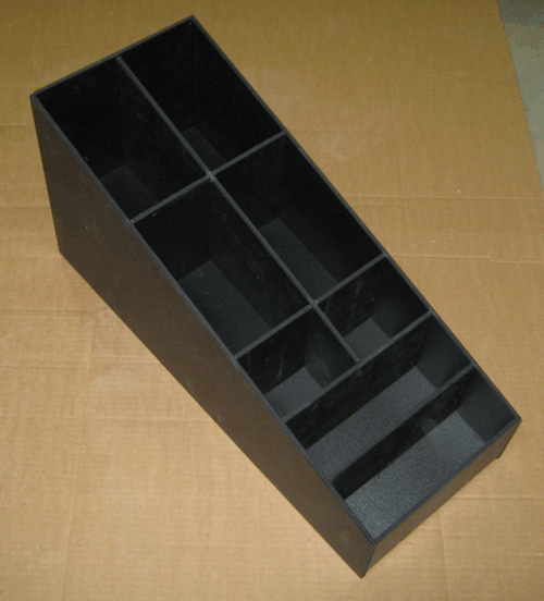 Black plastic storage tray with multiple compartments, viewed at an angle on a cardboard surface