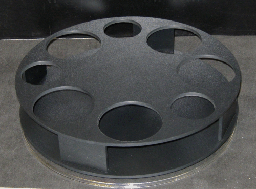 Black circular film reel with multiple round openings on a gray surface