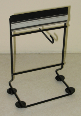 Black metal garment rack with a top shelf and four round feet against a plain wall