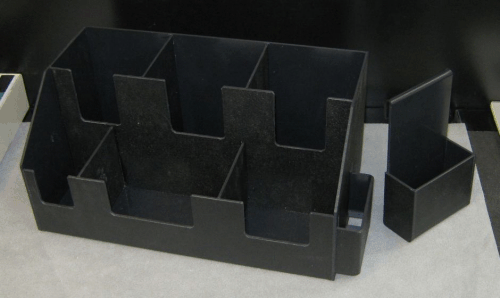 Black modular desktop organizer with several compartments and a separate matching piece on a gray surface