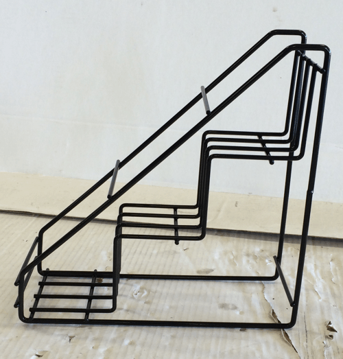 Black metal chair sculpture shaped like a staircase on a light floor against a white wall