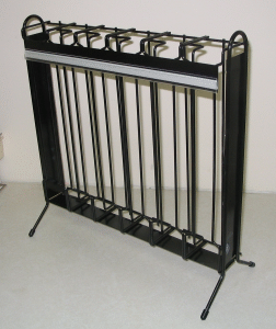 Black metal bicycle rack with multiple slots and support legs against a plain wall