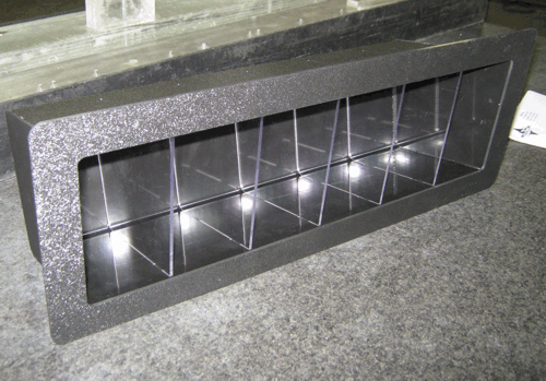 Black rectangular speaker cabinet with a row of reflective cone-like openings on a carpeted floor