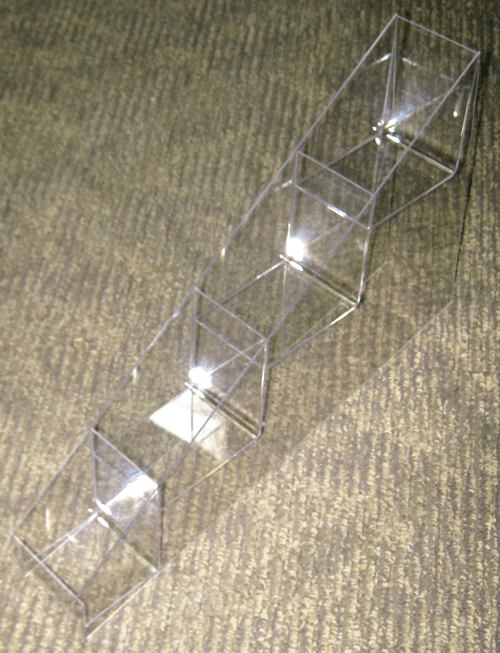 Clear acrylic geometric sculpture with connected cubes on a carpeted floor