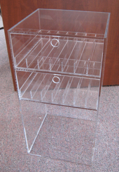 Clear acrylic countertop display rack with two slanted shelves and pull handles against a brown wall
