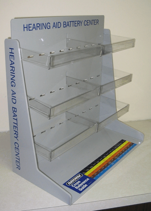 Clear acrylic display rack labeled “Hearing Aid Battery Center” with multiple shelves and blue base strip.