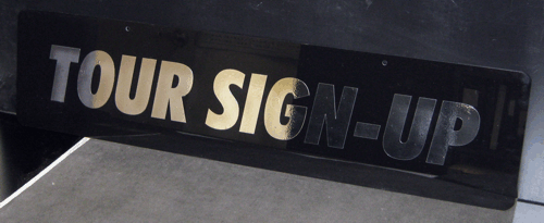 Black sign with bold white text reading “TOUR SIGN-UP”