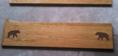 Two wooden plaques on a gray surface, each with a bear silhouette at the ends.