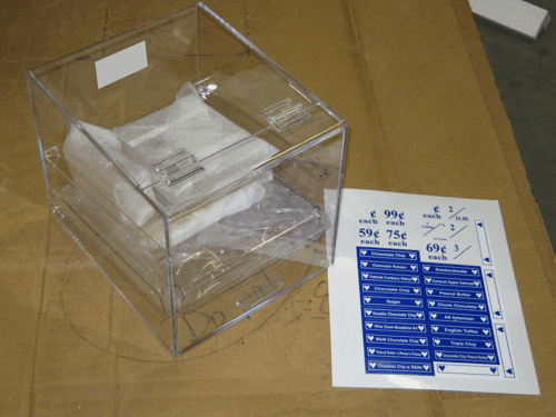 Clear plastic box with papers and a blue-and-white instruction sheet on a cardboard surface
