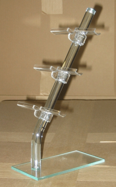 Clear acrylic display stand with three circular shelves on a glass base, holding a tilted metal rod