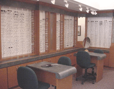 Quiet office with desks, chairs, and computer monitors beside windows with sheer curtains.