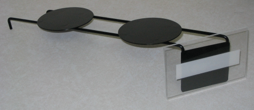 Metal eyeglasses with black temples and round lenses resting on a clear stand