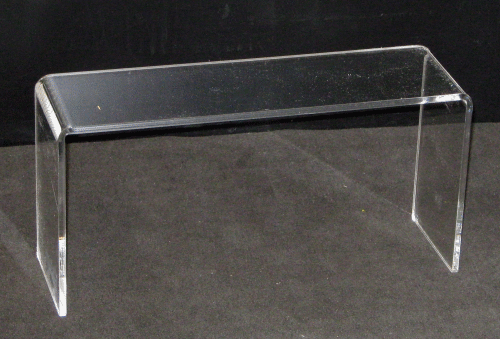 Transparent acrylic display stand with a clear rectangular top and two side supports on a dark background