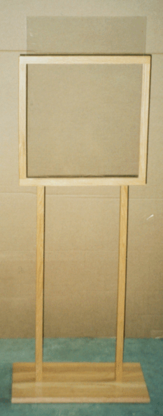 A wooden freestanding sign frame with a blank beige panel on a base against a plain wall.