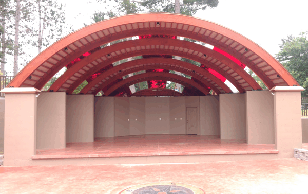 Empty outdoor stage with a red arched roof and beige columns in a park setting