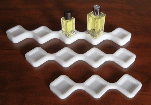 Three white wavy tray holders with small clear bottles of pale yellow liquid on the top tray.