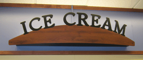 ICE CREAM sign on a wooden plank, arched black letters against a light wall