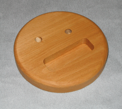 Round wooden lid with two small holes and a recessed handle slot on a gray surface