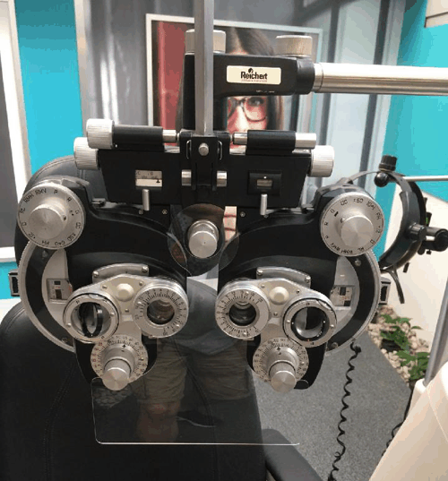 Close-up of an optometry phoropter with multiple dials and lenses mounted on an eye exam machine