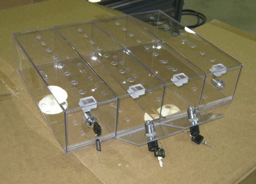 Clear acrylic box trap with black and silver mechanisms on a cardboard surface