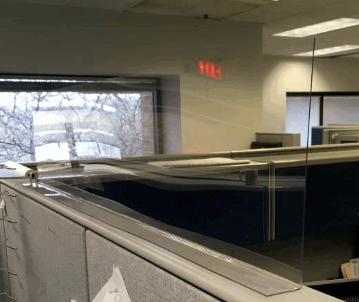 Office cubicles under fluorescent lights, with a window and red exit sign in the background.