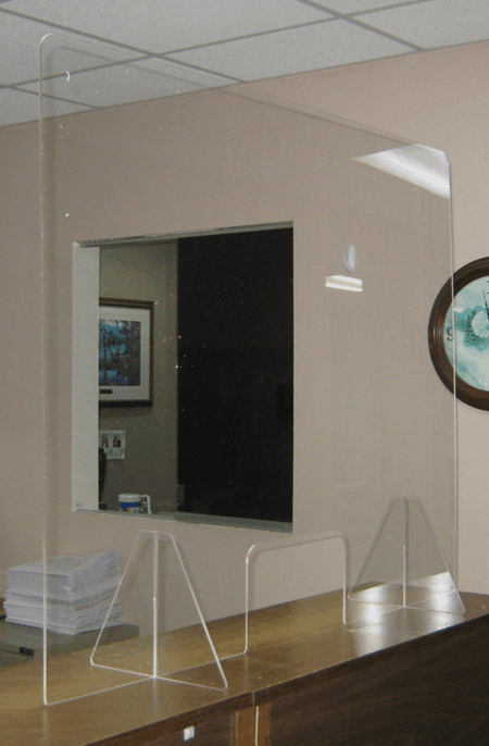 Office reception area with clear plexiglass barrier and a service window behind a wooden counter.
