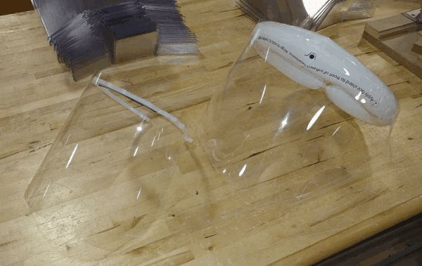 Broken clear plastic cups on a wooden table, with a black-and-white brush in the background