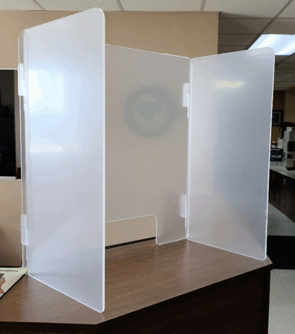 White three-panel desk privacy screen on a wooden table in an office setting