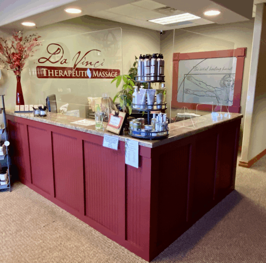 Massage therapy reception desk with red wood counter and spa products in a beige waiting area