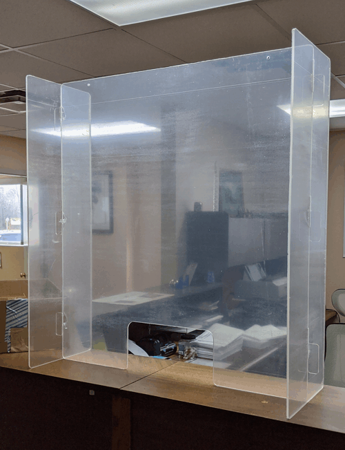 Clear plastic sneeze guard on an office counter with computers behind it